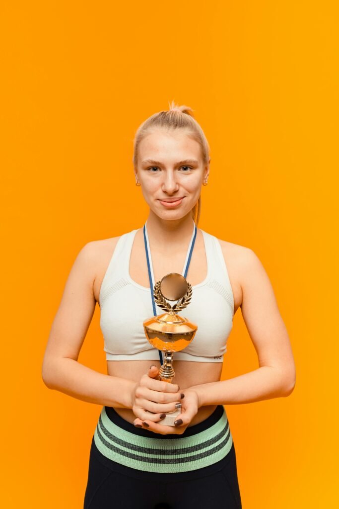 Smiling woman athlete holding a trophy in a studio with an orange backdrop, symbolizing victory.